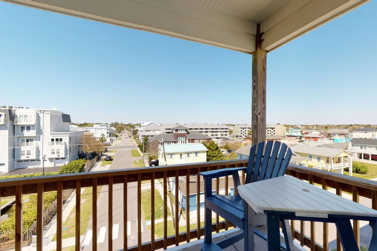 The image shows balcony seating overlooking a lively street scene, with surrounding houses in view. The vantage point suggests a perfect spot for morning coffee, evening relaxation, or people-watching, hinting at the social possibilities just outside the door.