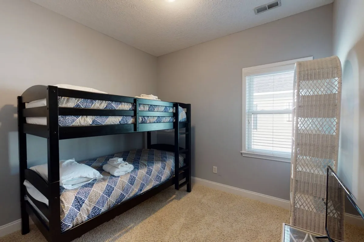 A cheerful bunk room featuring sturdy bunk beds, a window letting in natural light, and a soft floor rug. The inviting setup hints at a playful atmosphere perfect for children.