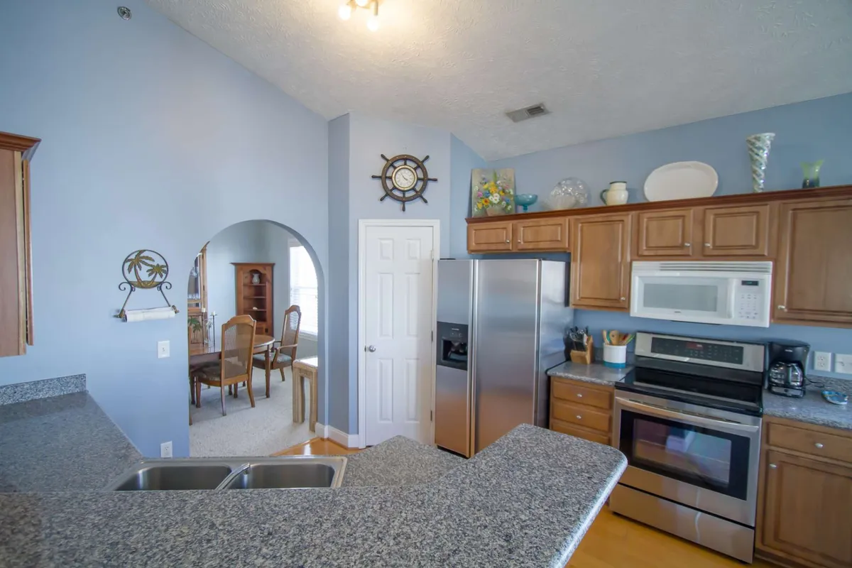 This interior shot offers a close view of a granite countertop and stainless steel appliances, with a welcoming dining area visible through an elegant archway. The layout encourages a sociable cooking and dining experience.