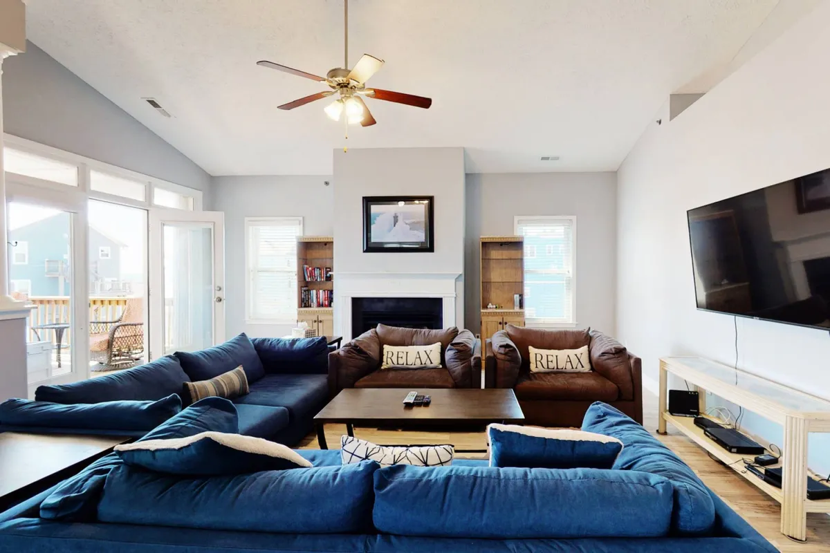 A spacious living room with comfortable sectional sofas arranged around a coffee table, a modern fireplace, and a television. Soft, natural light filters in, creating a warm and inviting atmosphere ideal for group gatherings and relaxation. The arrangement encourages conversation and communal activities, echoing the section’s focus on social spaces.